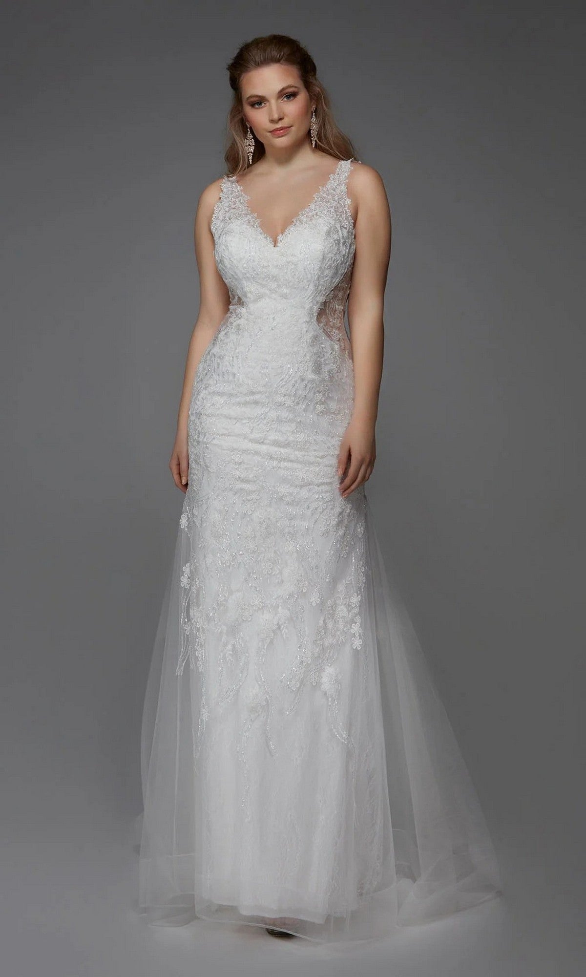 A woman wearing the Alyce 7017 Long White Dress in Diamond White, featuring a sleeveless lace design, V-neckline, sheer side panels, and a fitted silhouette, poses against a plain gray background.
